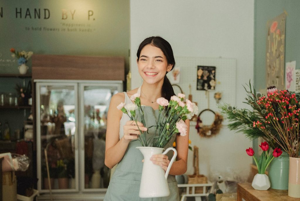 Crafting Captivating Headlines: Your awesome post title goes here Happy young female florist wearing apron standing with tender pastel carnation flowers in white vase while working in floristry store and looking away with charming smile